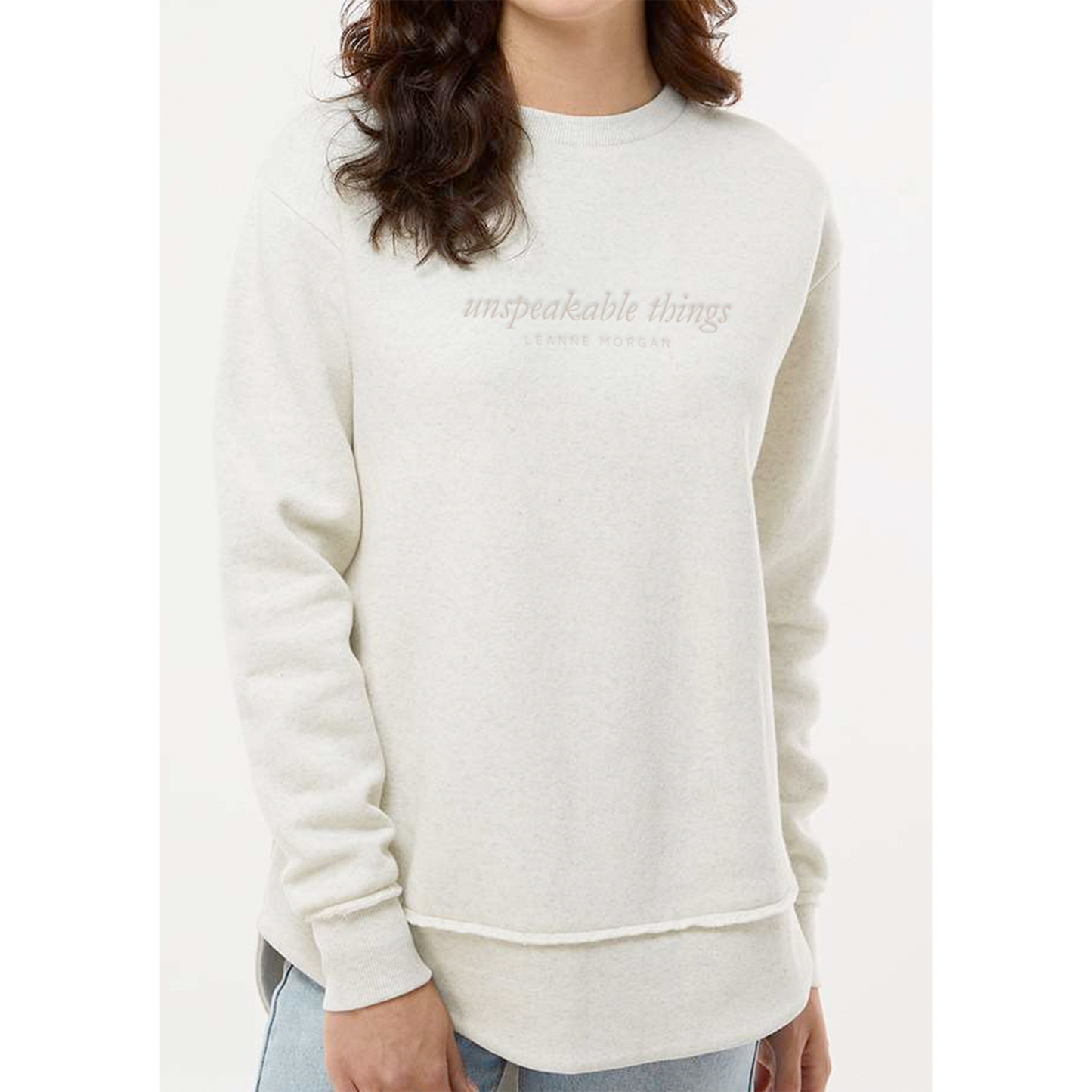 Person wearing a natural colored sweatshirt with text that says 'unspeakable things Leanne Morgan'on a white background