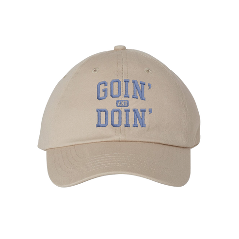 A beige baseball cap with 'GOIN' AND DOIN'' embroidered in blue on the front