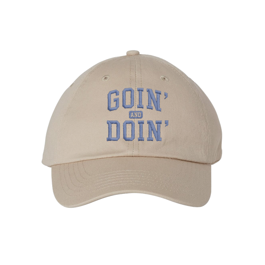 A beige baseball cap with 'GOIN' AND DOIN'' embroidered in blue on the front